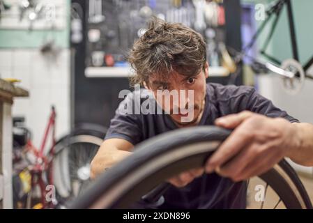 Riparatore di biciclette ispanico che installa uno pneumatico pieno senza aria su una ruota da bici in un'officina di riparazione. Composizione selettiva della messa a fuoco con spazio di copia. Foto Stock