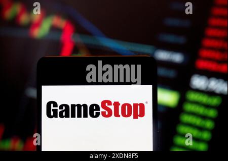 Cina. 23 giugno 2024. In questa immagine, il logo di GameStop Corp (NYSE: GME), il rivenditore americano di prodotti per videogiochi, elettronica di consumo e prodotti di gioco, è stato visualizzato su uno smartphone con un grafico dell'indice di borsa economica sullo sfondo. (Credit Image: © Budrul Chukrut/SOPA Images via ZUMA Press Wire) SOLO PER USO EDITORIALE! Non per USO commerciale! Foto Stock