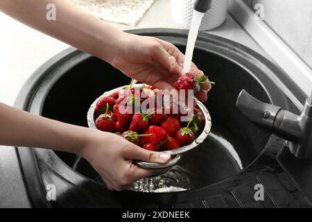 Donna che lava fragole fresche sotto l'acqua corrente in un colino metallico sopra il lavandino, primo piano Foto Stock