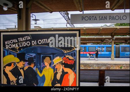 23 giugno 2024, Roma, Italia: un poster raffigurante l'inaugurazione della ferrovia Roma-Lido nel 1924 con lo slogan "nuovo percorso Roma Lido di Ostia" e, sullo sfondo, un treno moderno si fermò e una persona in attesa alla stazione di porta San Paolo per l'arrivo del prossimo treno per Ostia. Inaugurata nel 1924, la ferrovia urbana Roma-Lido è lunga 28,359 km e collega la stazione di porta San Paolo, nel quartiere Ostiense, alla stazione Cristoforo Colombo, nel quartiere Lido di Castel Fusano a Ostia, 10° comune di Roma, attraversando 13 stazioni di superficie. Nel 2022, la direzione passò a C. Foto Stock