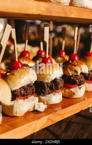 Primo piano di deliziosi mini hamburger con spiedini di legno e pomodori ciliegini su un vassoio di legno Foto Stock