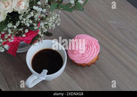 Torta alla panna e tazza di caffè. Un cucchiaio di caffè viene messo nella tazza da caffè. Nelle vicinanze si trova un bouquet di fiori in un vaso di vetro. Foto Stock