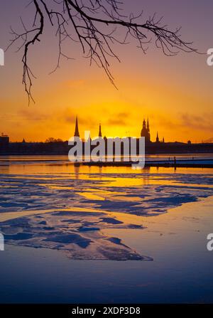Un bellissimo e colorato paesaggio all'alba con la silhouette dell'edificio centrale contro il luminoso cielo mattutino. Una lansdcape invernale con il fiume ghiacciato Daugava Foto Stock