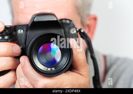 Uno scatto ravvicinato di una persona che tiene in mano una fotocamera digitale con un obiettivo di grandi dimensioni. La fotocamera è messa a fuoco sull'obiettivo, con la sfocatura del volto e del corpo delle persone Foto Stock