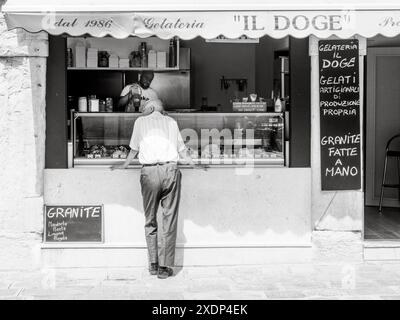 Venezia, Italia - 30 giugno 20220 uomo anziano che sceglie i sapori in una gelateria italiana, con un negoziante visibile all'interno Foto Stock