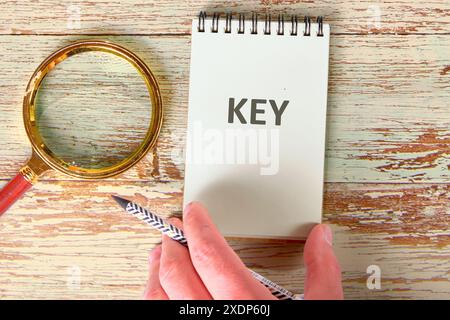 La CHIAVE di testo in un notebook con una mano sulla superficie accanto a una lente di ingrandimento Foto Stock