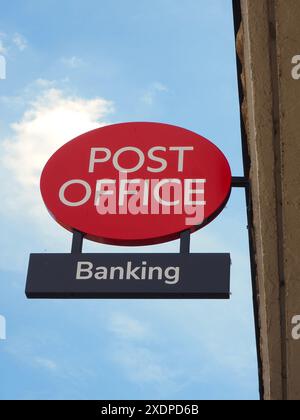 Ufficio postale britannico o britannico rosso e cartello bancario montato sulla parete sopra il punto vendita con sfondo blu leggermente nuvoloso. Foto Stock