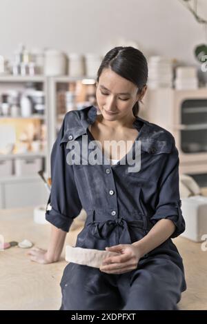 Artista ceramico asiatico seduto in studio con oggetti di argilla Foto Stock