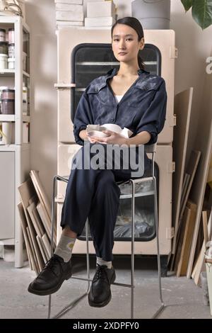 Artista ceramico asiatico seduto in studio Foto Stock