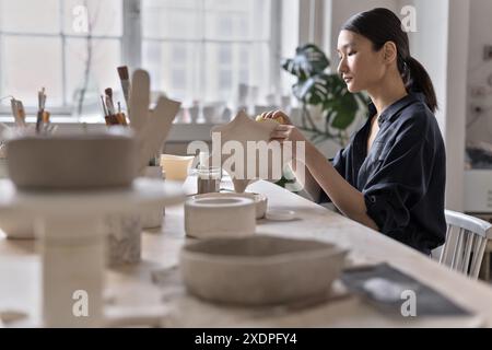 Artista asiatico lavora a un tavolo di lavorazione in uno studio di ceramica Foto Stock