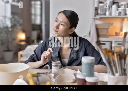 Artista asiatico lavora a un tavolo di lavorazione in uno studio di ceramica Foto Stock