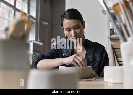 Artista asiatico lavora a un tavolo di lavorazione in uno studio di ceramica Foto Stock