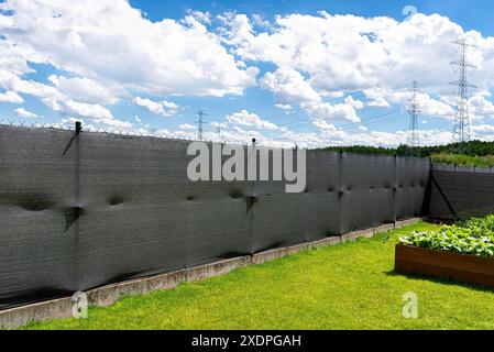 Rete di mascheratura color antracite posta su una recinzione a rete, scatole vegetali visibili. Foto Stock