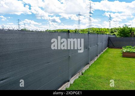 Rete di mascheratura color antracite posta su una recinzione a rete, scatole vegetali visibili. Foto Stock