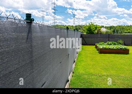 Rete di mascheratura color antracite posta su una recinzione a rete, scatole vegetali visibili. Foto Stock