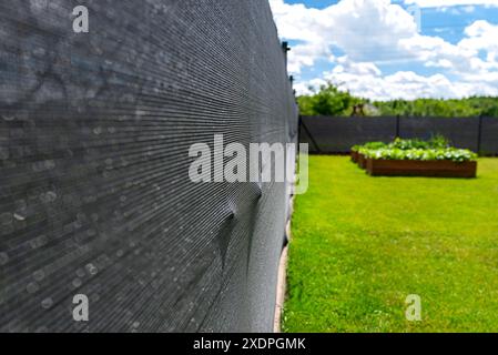 Rete di mascheratura color antracite posta su una recinzione a rete, scatole vegetali visibili. Foto Stock