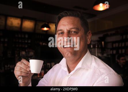 Uomo che tiene una piccola tazza di caffè e sorride all'interno di un bar Foto Stock