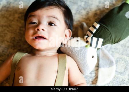Il bambino è disteso su una superficie morbida con un giocattolo imbottito accanto. Foto Stock