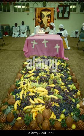 Una cerimonia di battesimo, un battesimo, i membri della chiesa hanno appena ballato intorno all'enorme mucchio di frutta. Ci sono sette tipi di frutta e le bambine ottavo giorno di vita. Nel mezzo del gruppo un bambino è tenuto dalla Profetessa, che è nello Spirito. Alla sua sinistra uno "scriba" traduce le "profezie e le scrive tutte. Parla in lingue che è uno dei doni soprannaturali dello Spirito Santo. Il padre dei bambini registra tutto su un registratore. Elephant and Castle, Londra, Inghilterra, 1993 1990 UK HOMER SYKES Foto Stock