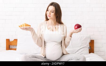 Donna incinta scegliendo tra un croissant e Apple Foto Stock