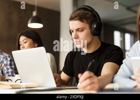 Giovane uomo che indossa le cuffie e si concentra sul laptop Foto Stock