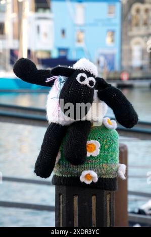 La stravagante figura di lana all'uncinetto del personaggio di "Shaun the Sheep" della Aardman Animations copre la parte superiore di un dissuasore di metallo. Weymouth, Dorset, Inghilterra, Regno Unito Foto Stock