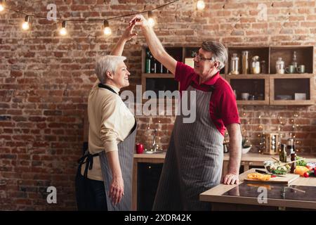 Coppia senior che balla nella cucina moderna con luci a corda Foto Stock