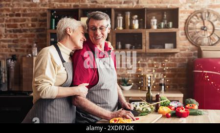 Coppia anziana che cucinano insieme nella loro cucina, abbracciano Foto Stock