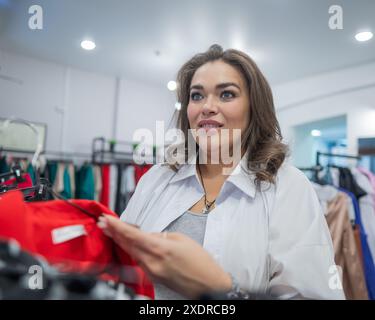 Una donna grassa guarda con orrore al prezzo di un abito in un negozio Plus size. Foto Stock