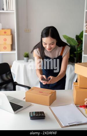 Giovane donna che prepara pacchi per il business online con notebook e calcolatrice in Modern Workspace Foto Stock