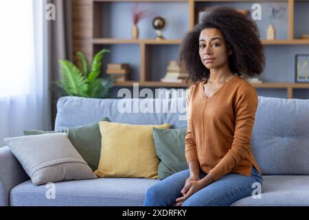 Giovane donna sicura che siede sul divano in un moderno soggiorno con arredi eleganti. Atmosfera rilassata e tranquilla. Luce naturale per creare un'atmosfera accogliente. Foto Stock