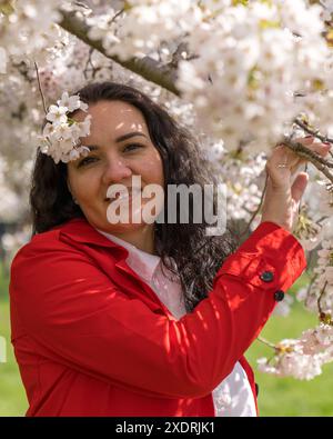 immagine romantica di una donna elegante con un cappotto rosso e una camicetta bianca. Umore positivo. Una ragazza carina tiene delicatamente un ramo sakura bianco e guarda la cameriera Foto Stock