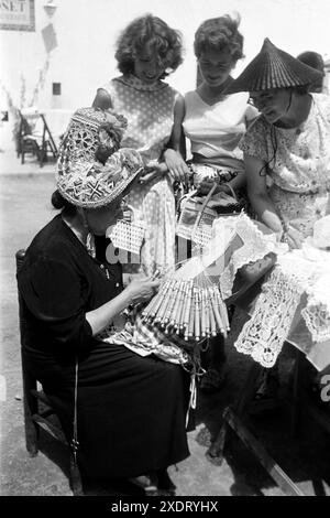 Frauen gucken einer Dame in Tracht beim Klöppeln von Spitze zu, Tossa de Mar 1957. Donne che guardano una signora in costume tradizionale merletto, Tossa de Mar 1957. Foto Stock