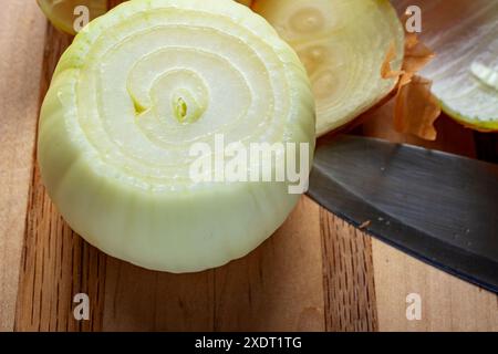 Una cipolla gialla appena sbucciata siede su un tagliere di legno con un coltello nelle vicinanze. Foto Stock