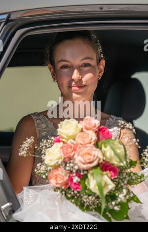 Una giovane e bella sposa in macchina tiene in mano un bouquet di nozze Foto Stock