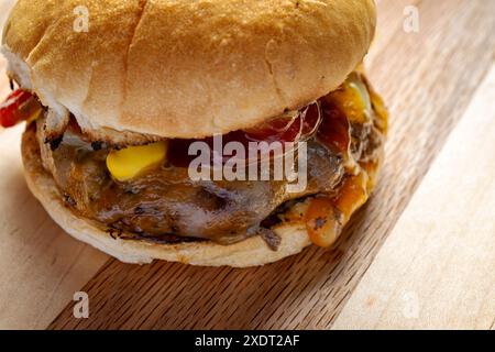 Direttamente dalla griglia, hamburger con formaggio cojack, cipolle grigliate, sottaceti di aneto, ketchup e senape su un panino tostato. Su un boa di legno Foto Stock