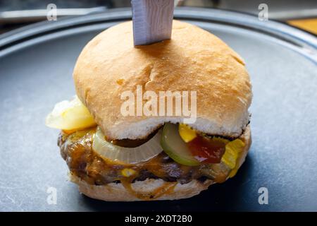 Direttamente dalla griglia, hamburger con formaggio cojack, cipolle grigliate, sottaceti di aneto, ketchup e senape su un panino tostato. Su un piatto con Foto Stock