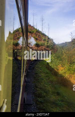 Treno a vapore d'epoca che gira dietro un angolo e si riflette sulle montagne Cambriane del Galles Foto Stock