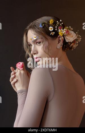 Una donna con dei fiori tra i capelli e sul viso guarda lontano dalla telecamera mentre tiene in mano una piccola rosa. Foto Stock