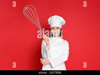 Buon pasticcere con grande frusta su sfondo rosso Foto Stock