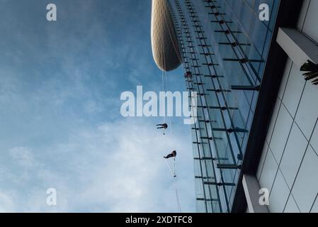 Gli addetti alla pulizia professionale delle finestre scorrono lungo la facciata di vetro del Marina Bay Sands Hotel a Singapore, eseguendo lavori di manutenzione di alti piani sullo sfondo Foto Stock