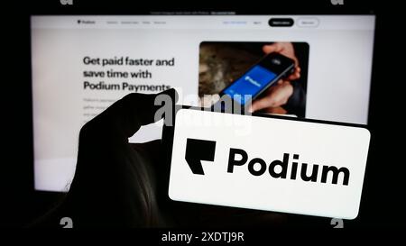 Persona che possiede uno smartphone con il logo della società di software statunitense Podium Corporation Inc. Davanti al sito Web. Mettere a fuoco il display del telefono. Foto Stock