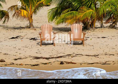 Due sedie di legno vicino al bordo dell'acqua su una spiaggia coperta di legno. Niente persone. Concetto di vacanza. Foto Stock