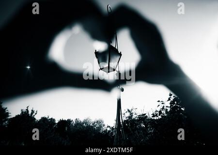 Una fotografia in bianco e nero di un viaggiatore, che mostra un simbolo del cuore creato con le mani, guarda un'antica lanterna alla luce del sole. L'immagine CA Foto Stock