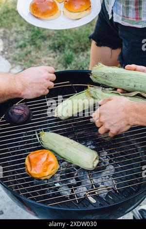 tre persone alla griglia a carbone: barbecue estivo, barbecue con pannocchie, hamburger, panini Foto Stock