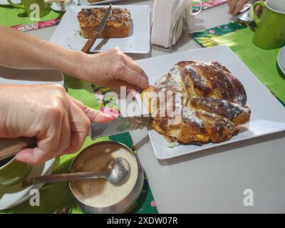 Spuntino con yogurt e pane al sesamo, ciambelle, tazza verde, tovaglioli, latte, cucchiaio, tovaglioli, zucchero e le mani di una donna che rompono la ciambella. Foto Stock