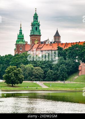 Il Castello di Wawel si erge maestosamente sopra le rive del fiume Vistola in una soleggiata giornata estiva, con il verde che circonda lo storico monumento polacco. Cracovia, Polonia Foto Stock