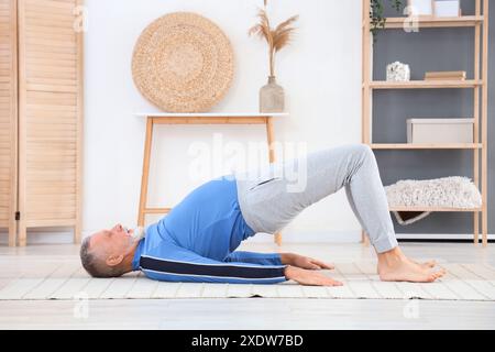 Uomo maturo sportivo che fa yoga su tappeto a casa Foto Stock