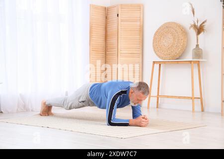 Uomo maturo sportivo che fa yoga su tappeto a casa Foto Stock