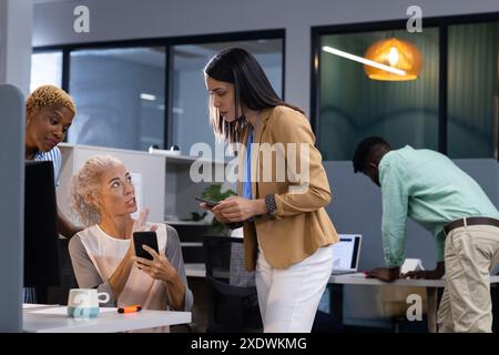In ufficio, donna d'affari che mostra lo smartphone ai colleghi, discutendo di un progetto di lavoro Foto Stock